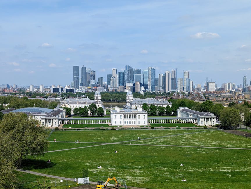 A panoramic view of a large, historic white building with classical architecture, including columns and decorative features, situated in a well-maintained green park with trimmed grass, walking paths,