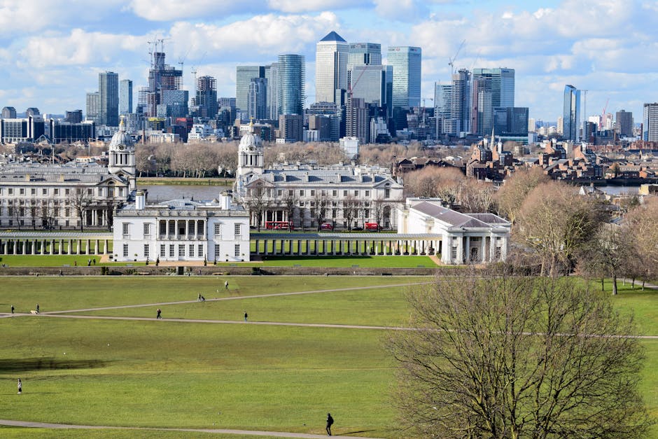 A panoramic view of a large, historic white building with classical architecture, including columns and decorative features, situated in a well-maintained green park with trimmed grass, walking paths,